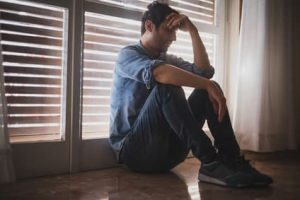 Understanding substance use and stress. Man looking upset sitting on the floor